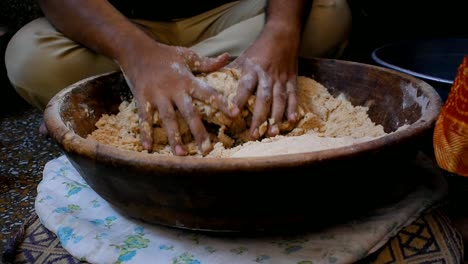 man kneading flour dough with both hands in a wooden plate placed on cotton cloth