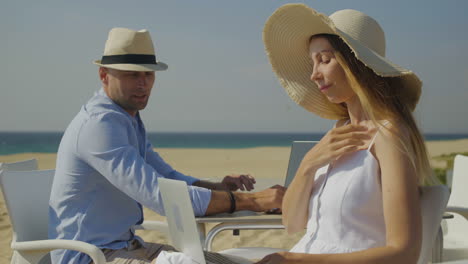 young couple using laptops on beach