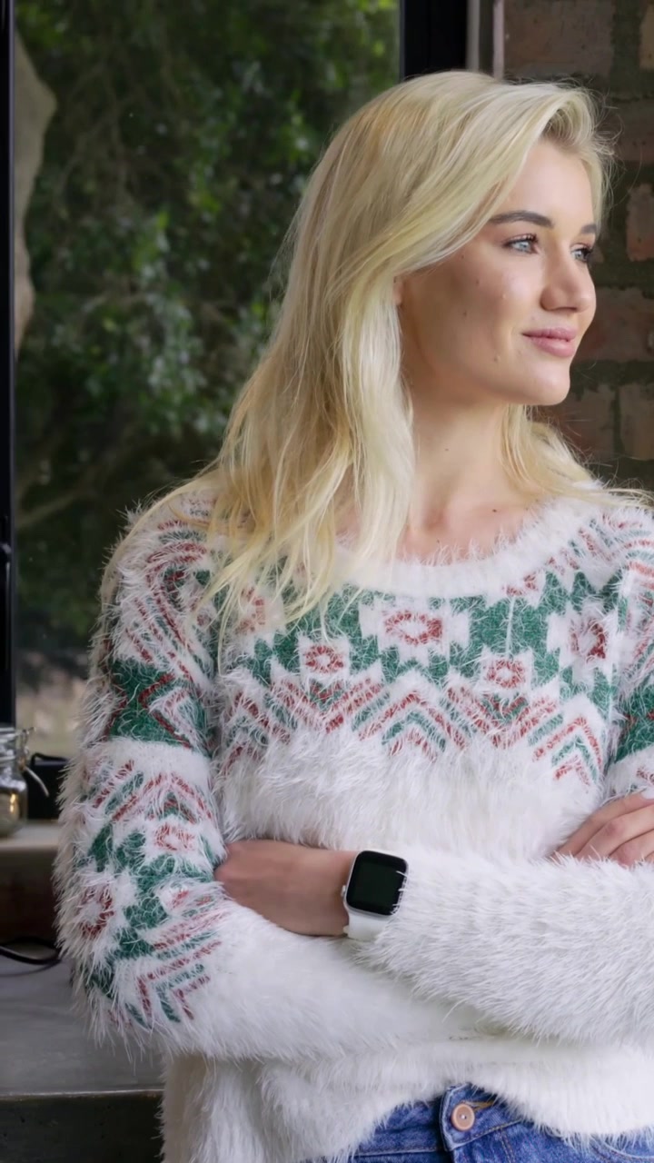 Lodret video: Kvinde i sweater i køkkenet ser ud i haven, vender sig mod vinduet med krydsede arme og smartwatch.