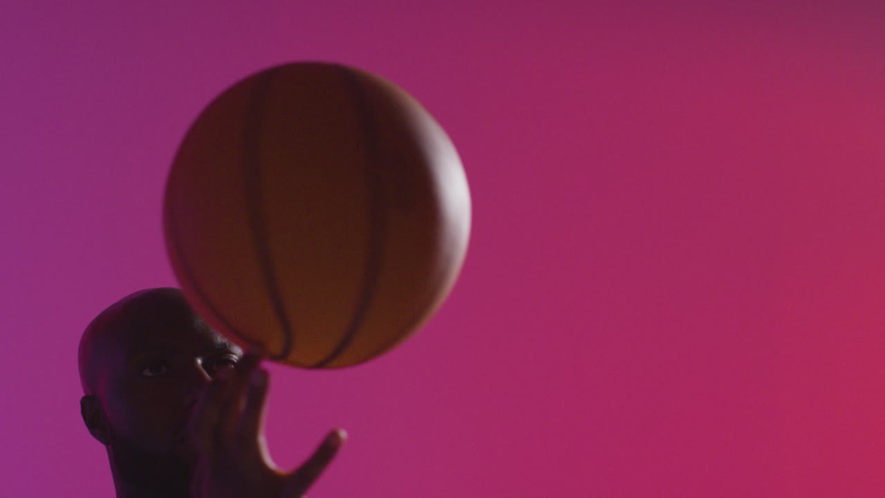 близкий студийный снимок мужского баскетболиста, вращающего мяч на пальце на розовом освещенном фоне 1