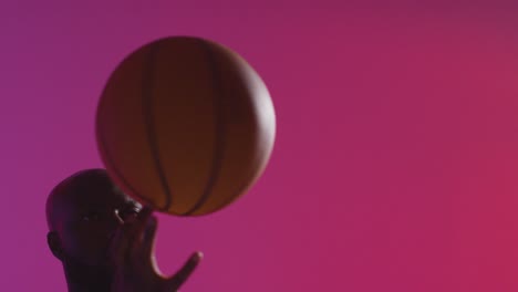 Nahaufnahme-Eines-Männlichen-Basketballspielers,-Der-Den-Ball-Am-Finger-Vor-Rosa-Beleuchtetem-Hintergrund-Dreht-1