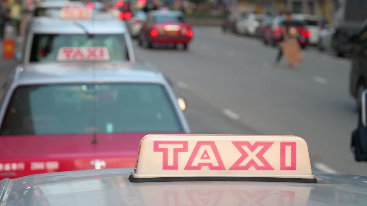 En række taxaer med oplyste skilte på motorhjelmen, parkeret i vejkanten og ventende på kunder