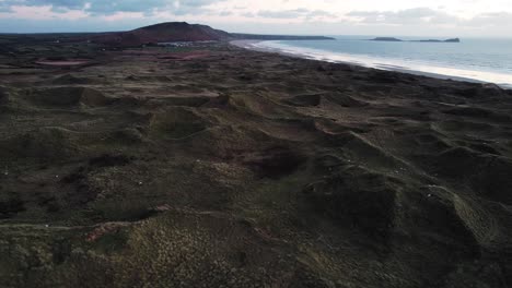 AERIAL:-Slow-pan-over-textured-landscape-towards-Rhossili-beach,-Gower,-4k-Drone