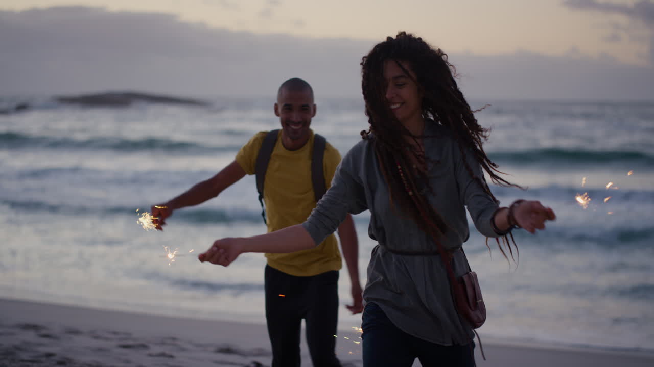 happy diverse friends on beach dancing celebrating new years eve waving sparklers enjoying silly fun together in calm ocean seaside background at sunset