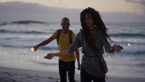 Fröhliche,-Vielfältige-Freunde-Am-Strand,-Die-Tanzen-Und-Silvester-Feiern,-Wunderkerzen-Schwenken-Und-Gemeinsam-Albernen-Spaß-Vor-Dem-Hintergrund-Des-Ruhigen-Meeres-Am-Meer-Bei-Sonnenuntergang-Genießen