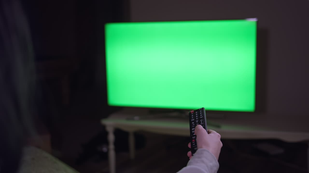 A girl with a remote control in her hand switches channels, sits at night near the TV
