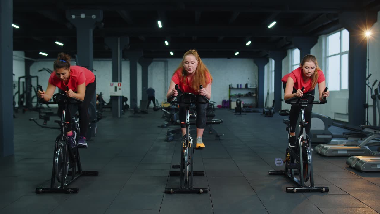 Athletic women group riding on spinning stationary bike training routine in gym weight loss indoors