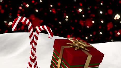 Digital-animation-of-christmas-candy-cane-and-gift-box-on-snow-against-red-spots-of-light-against-bl