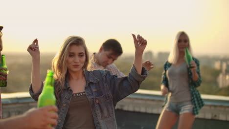 the young girl is dancing on the roof with her friends on the party. she closes her eyes and enjoys the time in shorts and a light denim jacket in summer everning. her blond hair is flying in the wind. she is dancing with her arms and body.