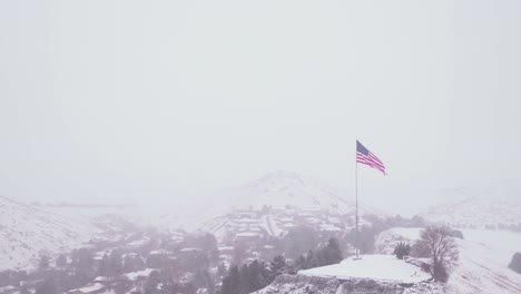 aerial view of a large american flag waving on top of a mountain during a blizzard