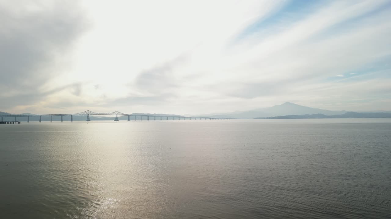 Low angle drone footage of the Richmond–San Rafael Bridge illuminating the waters near Point Molate Beach.