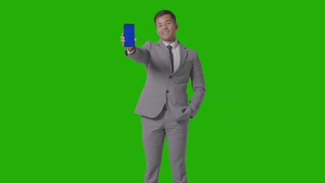 studio shot of smiling businessman in suit holding blue screen mobile phone against green screen 1