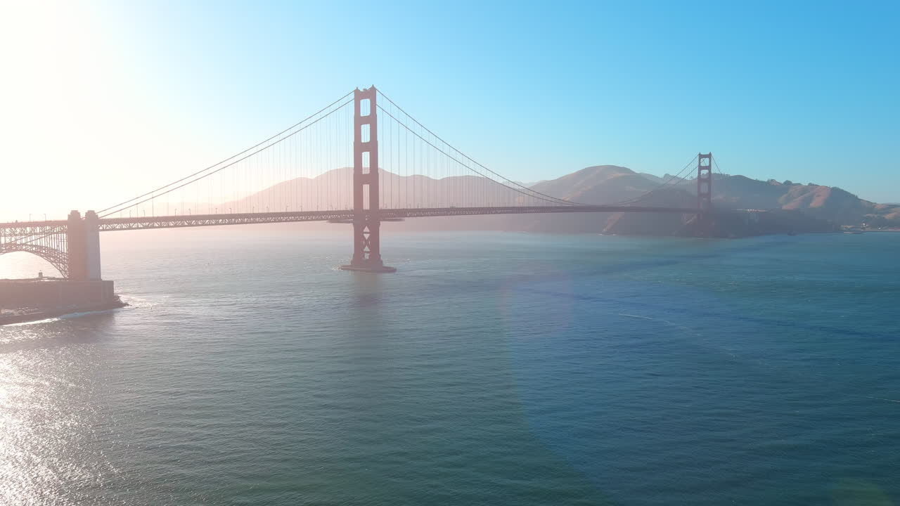 Cinematic pan right of the Golden Gate Bridge at sunset, with soft haze over San Francisco Bay and view toward Marin
