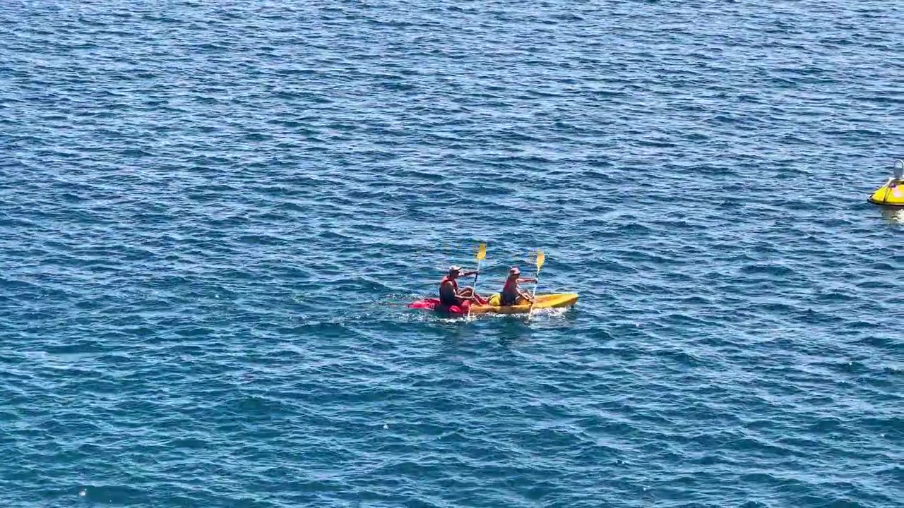 Due canoisti remano attraverso il blu intenso del Mar Mediterraneo durante una soleggiata giornata estiva.
