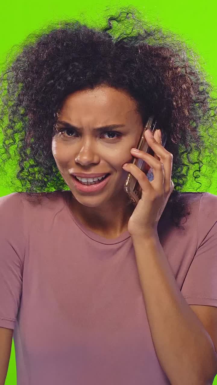 Surprised young woman talking on the phone against a bright green background