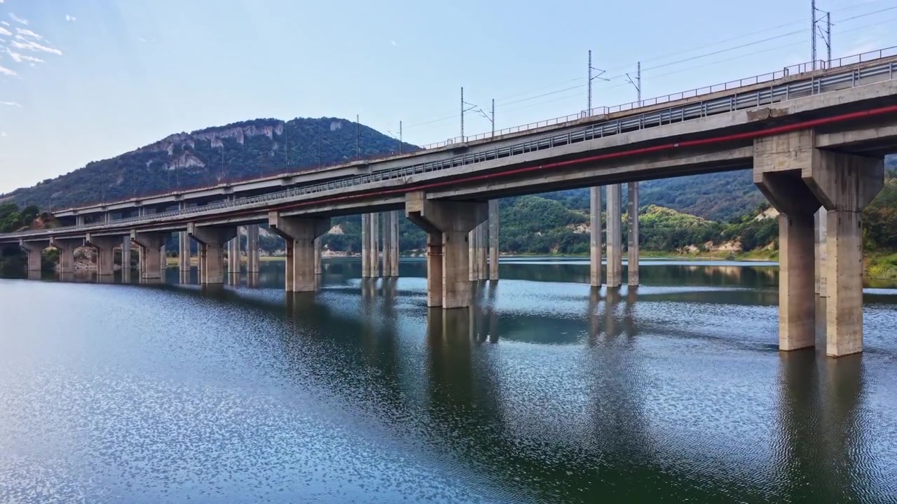 Ponte che attraversa uno specchio d'acqua con riflessi e montagne sullo sfondo durante una giornata limpida