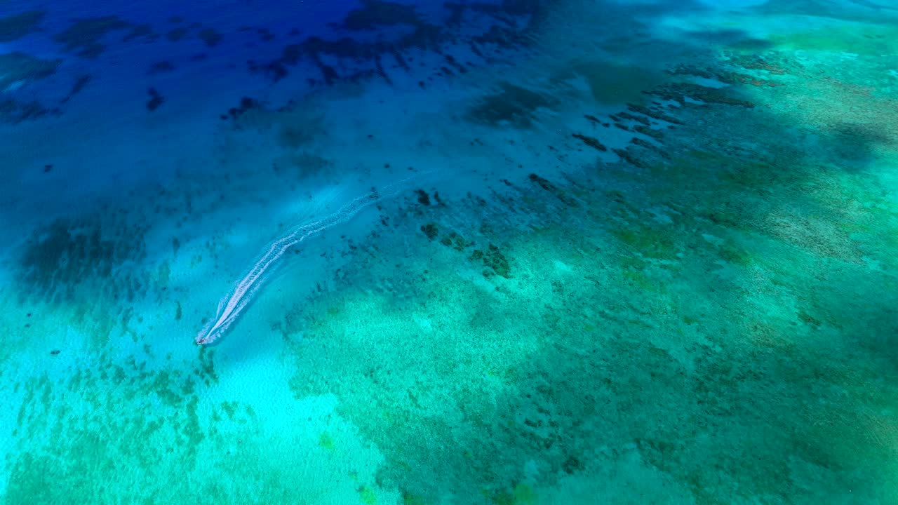 Aerial follow of boat cruising through cloud-shadowed turquoise Caribbean off Grand Cayman
