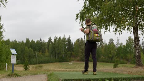 Disc-golfer-steps-onto-the-tee-and-puts-bag-down---Wide-shot