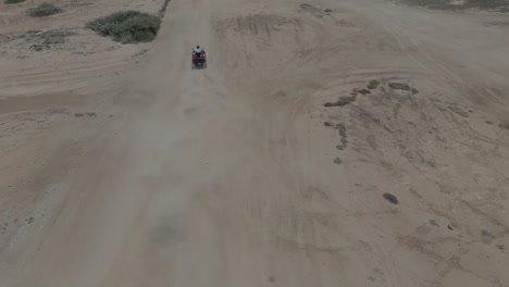 AERIAL:-Drone-shot-of-a-person-riding-an-ATV-in-sand