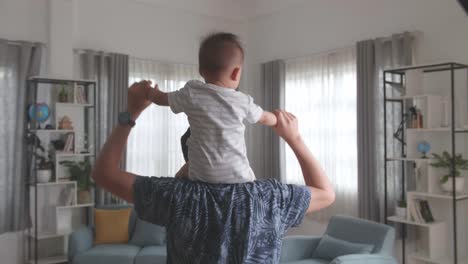 little son sitting on the parent's shoulders walking at home