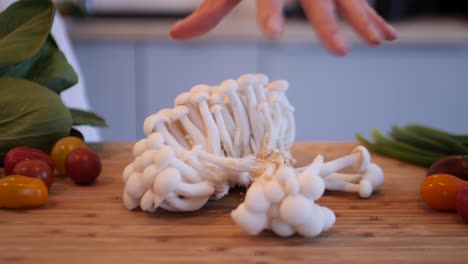 primer plano de una mujer sosteniendo el hongo enoki y al soltarlo, diferentes vegetales alrededor
