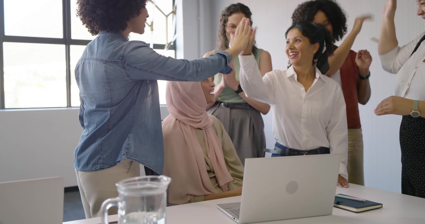 Equipe feminina diversa reunida em torno de uma mulher de hijab após apresentar um gráfico no laptop, aplaudindo no escritório.