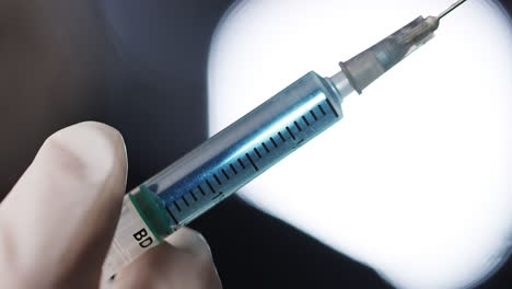 handheld close up of gloved hand holding syringe