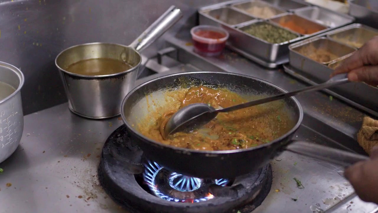 Nærbillede af en kok, der rører krydret kyllingecurry i en wok på et professionelt komfur