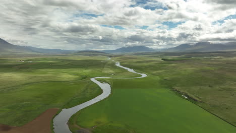 river in iceland flowing in farmlands aerial shot cloudy day with mountains