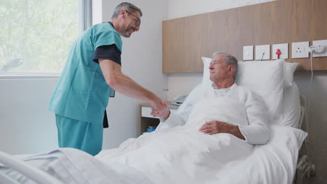 surgeon visiting and shaking hands with senior male patient in hospital bed in geriatric unit