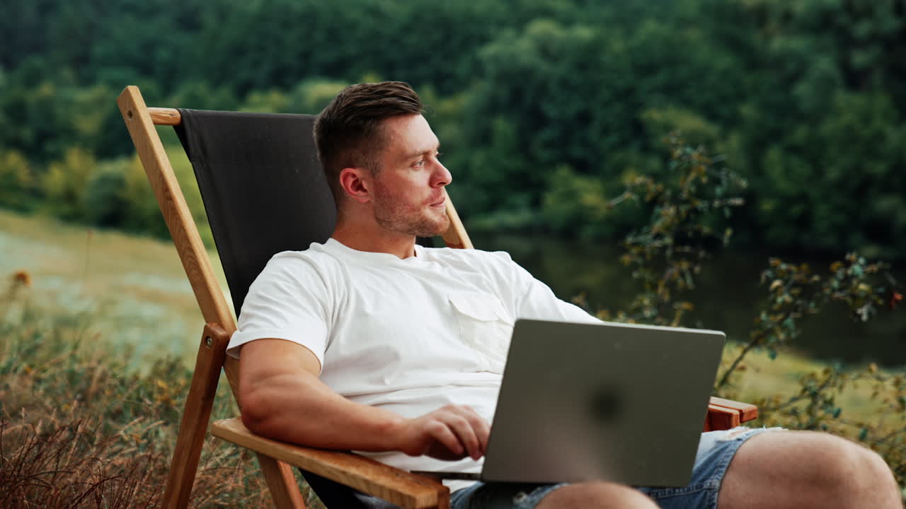 Caucasian bearded mid-aged man distracts from work on laptop. Businessman freelancer looks away thinking of something.
