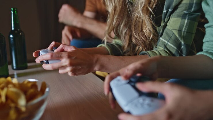 Friends hands holding joysticks playing video game at home sofa close up.