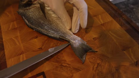 chef skilfully slicing fish tail on wooden chopping board