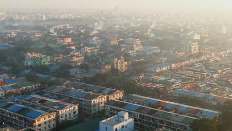 Drone-trucking-shot-of-a-giant-bus-station-in-Mandalay,-Myanmar-on-a-hazy-morning-during-sunrise