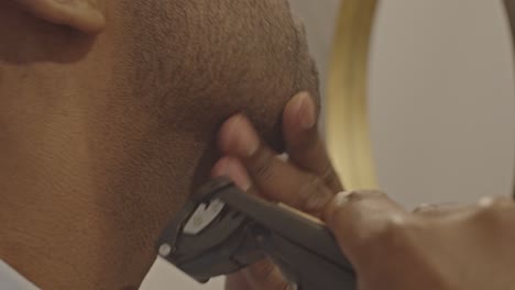 close up of man using trimmer to shave his face while light flares in the camera lens