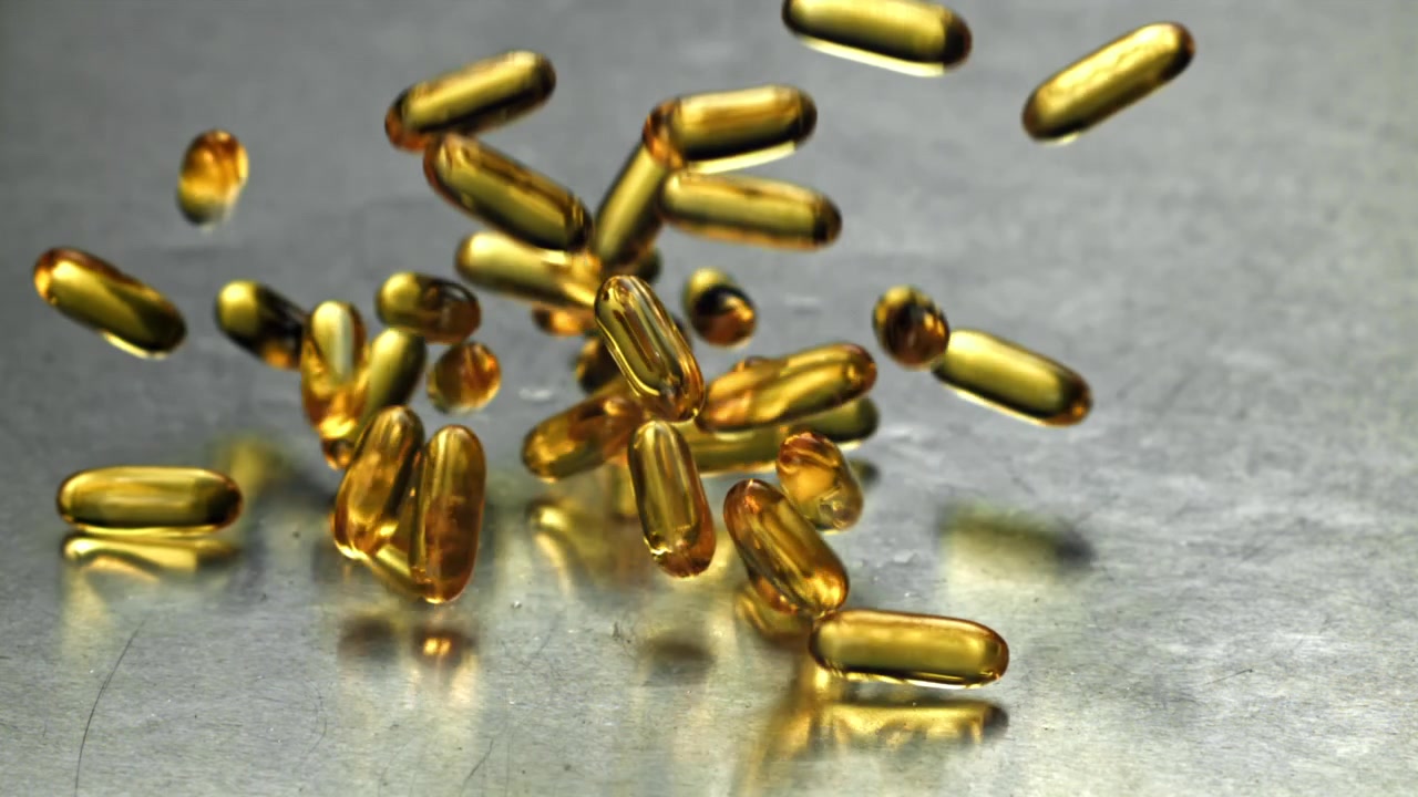 Capsule Omega 3 dorate che cadono al rallentatore su superficie metallica