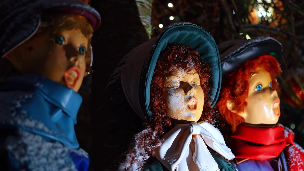 Close-up dos rostos de estátuas vintage de cantores de Natal ao ar livre. Tomada macro de figuras natalinas cantando com neve nos rostos e chapéus de inverno sob iluminação noturna em Nova York.