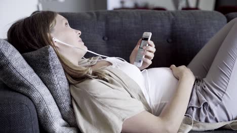 smiling pregnant woman having video call while lying on sofa