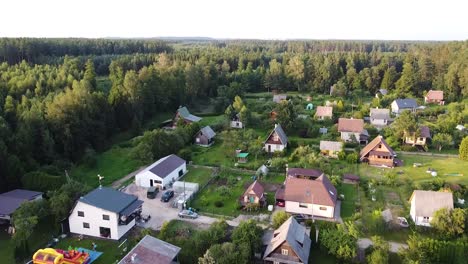 Cozy-small-village-surrounded-by-woodlands,-aerial-ascend-view