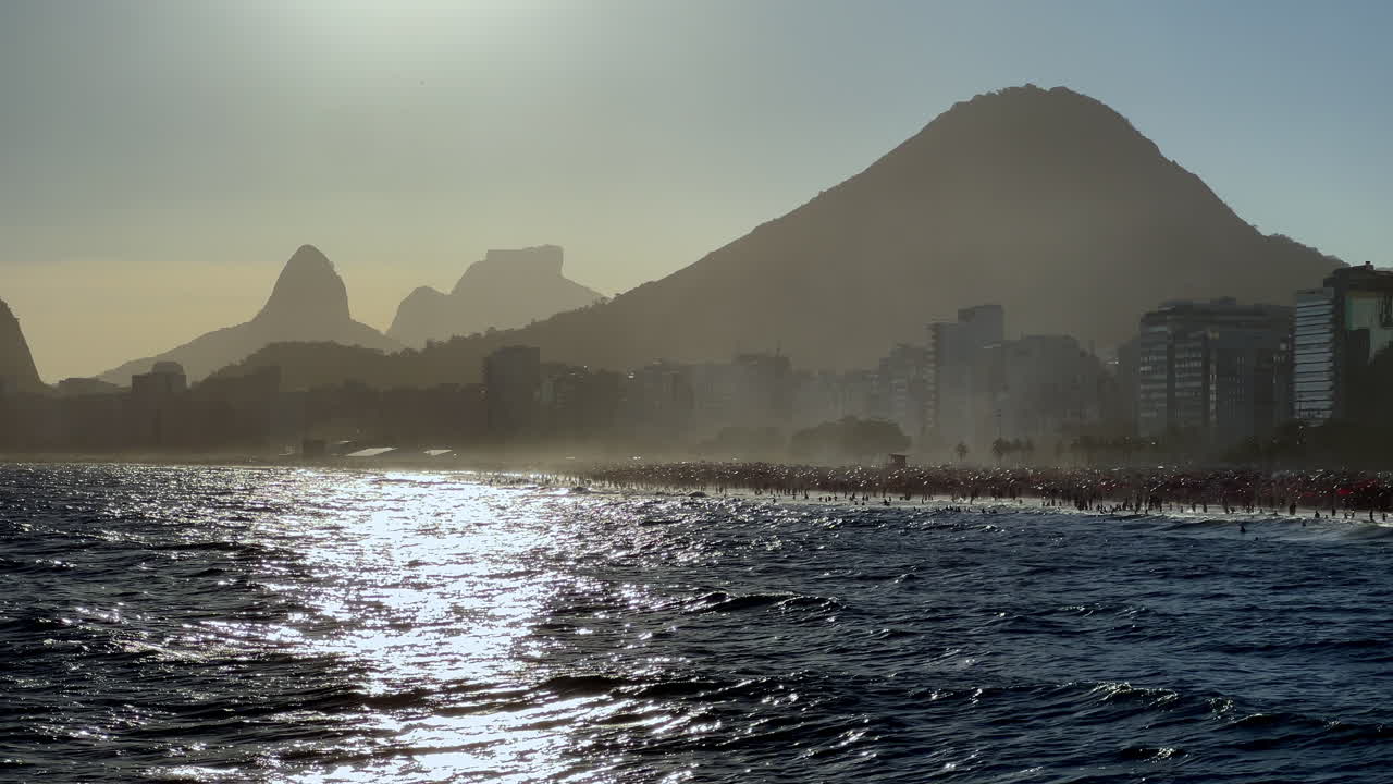 Cinematische weergave van de zonsondergang die weerkaatst op de zee in Rio de Janeiro. Met de gouden gloed die schittert op de golven met de silhouetten van de Suikerbroodberg en de skyline van Copacabana op de achtergrond