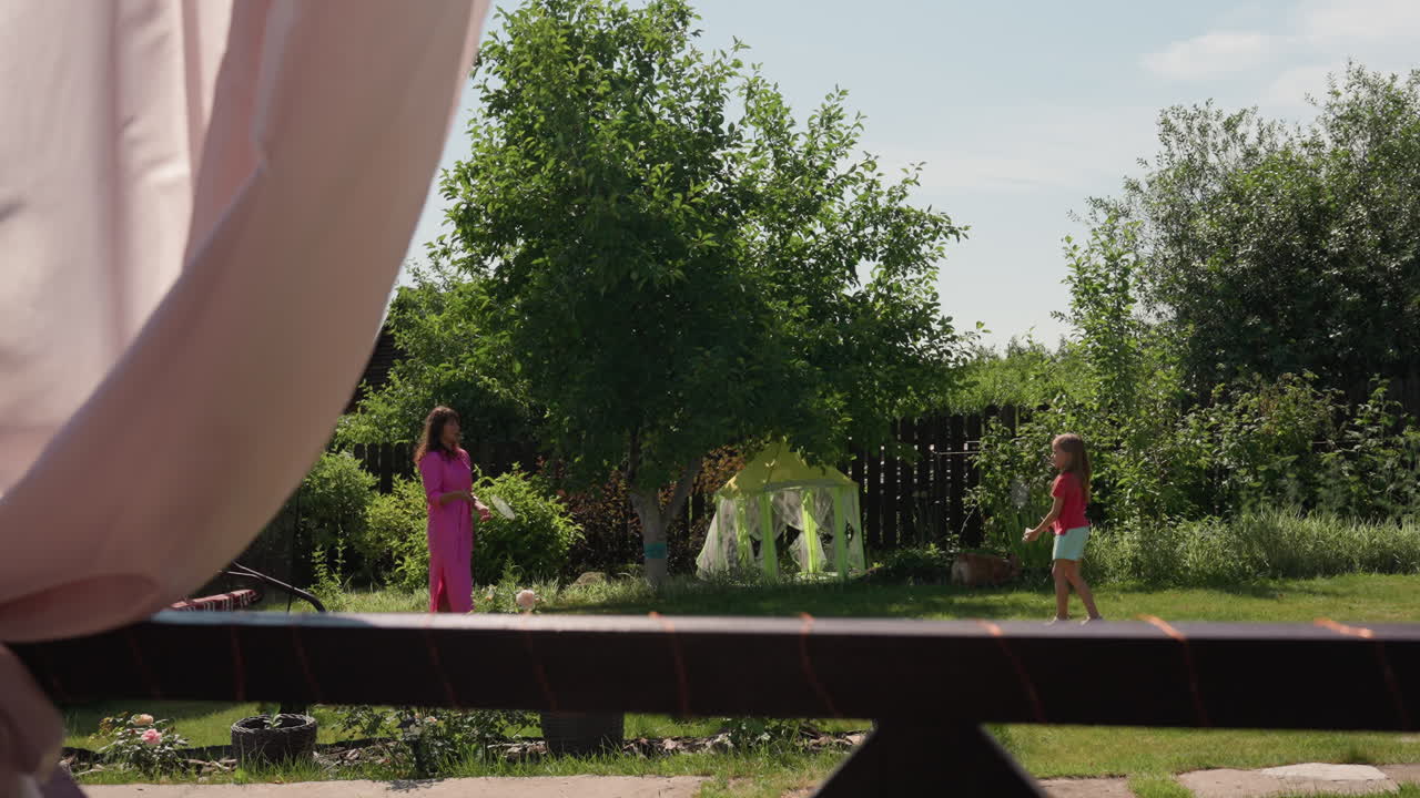 CurtainEdge Garden White Mother Chatting With Daughter, Play Tent Under Tree, Relaxed Backyard Stroll, Sunlight On Fence And Grass, Casual Summer Family Moment, Soft Conversation