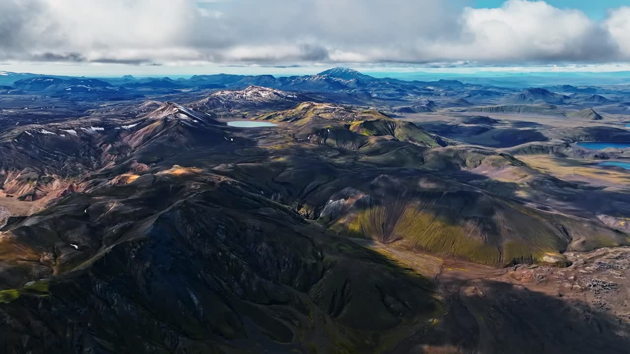 Aerial sweep over Landmannalaugar’s colorful rhyolite ridges and winding glacial rivers, captured near cloud level above Iceland’s vibrant volcanic highlands