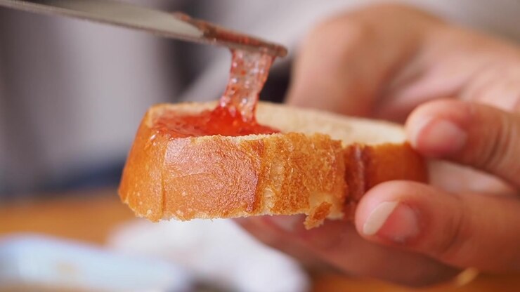 Spreading Strawberry Jam on a Slice of Fresh Bread