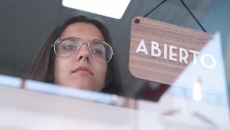 young sad woman changing open to closed sign in spanish on window for corona virus pandemic.