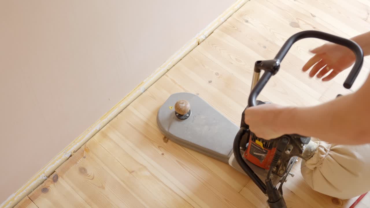 Person Operating Floor Sanding Machine On Wooden Flooring Near Wall. overhead shot. Turning off.