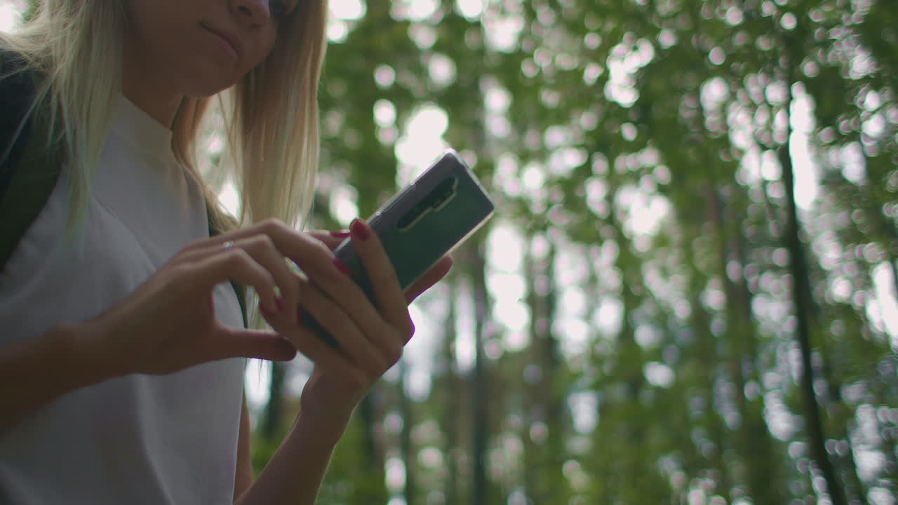 primer plano de una mujer con un teléfono móvil caminando por el bosque viajando con una mochila en cámara lenta. navegar por el bosque usando el navegador en su teléfono móvil