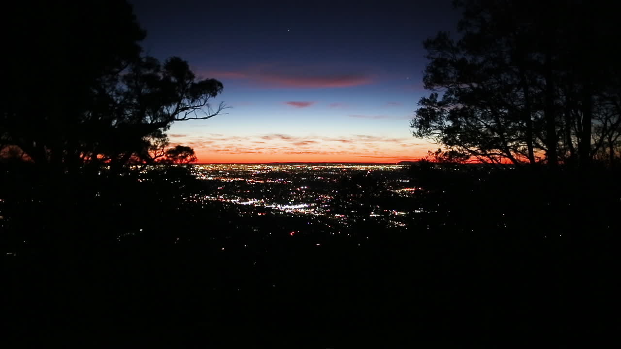 impresionante vista al atardecer de la expansión urbana de la ciudad vista a través de una ruptura en la silueta de la línea de árboles de montaña