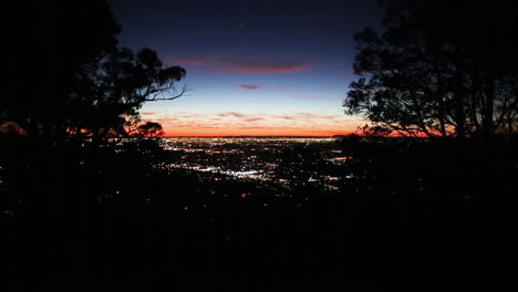 stunning dusk view of city urban sprawl as seen through a break in mountain tree line silhouette view