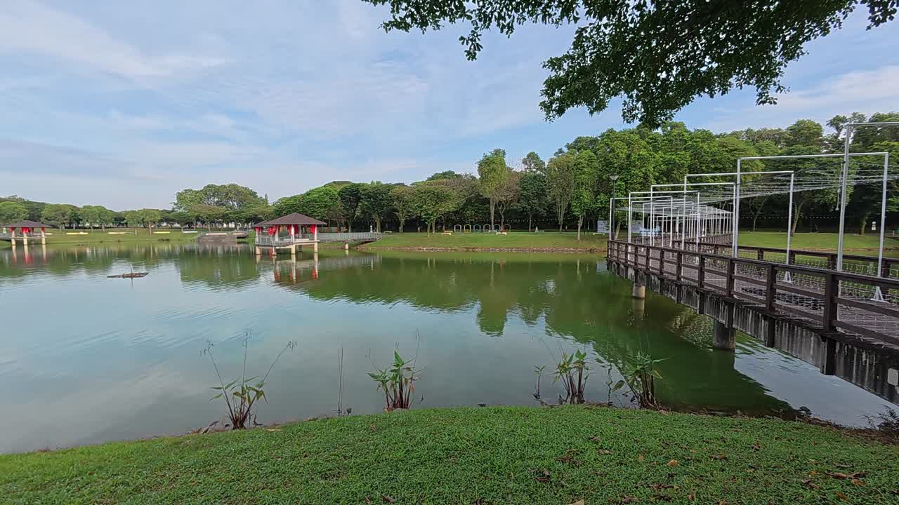 A tranquil lake in a tropical public park surrounded by lush greenery. Visitors enjoy recreation and relaxation in this serene setting.