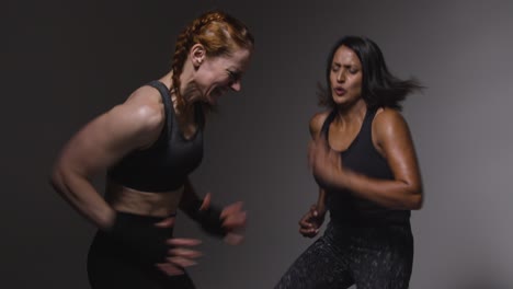 studio shot of two mature women wearing gym fitness clothing doing cardio exercise running on the spot together